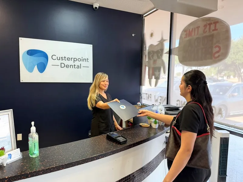 A patient checks in at the front desk in front of the navy logo wall